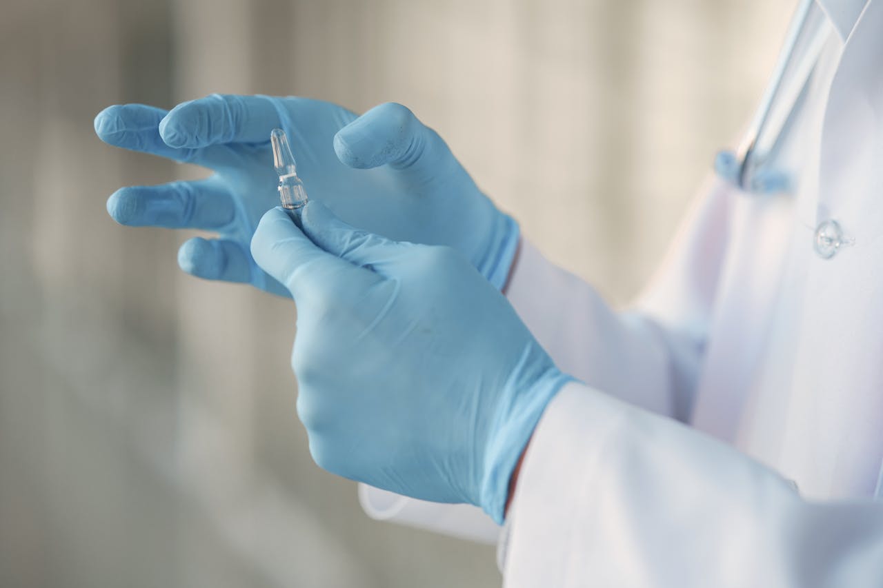 About Close-up of a healthcare professional in gloves holding a glass vaccine ampoule.