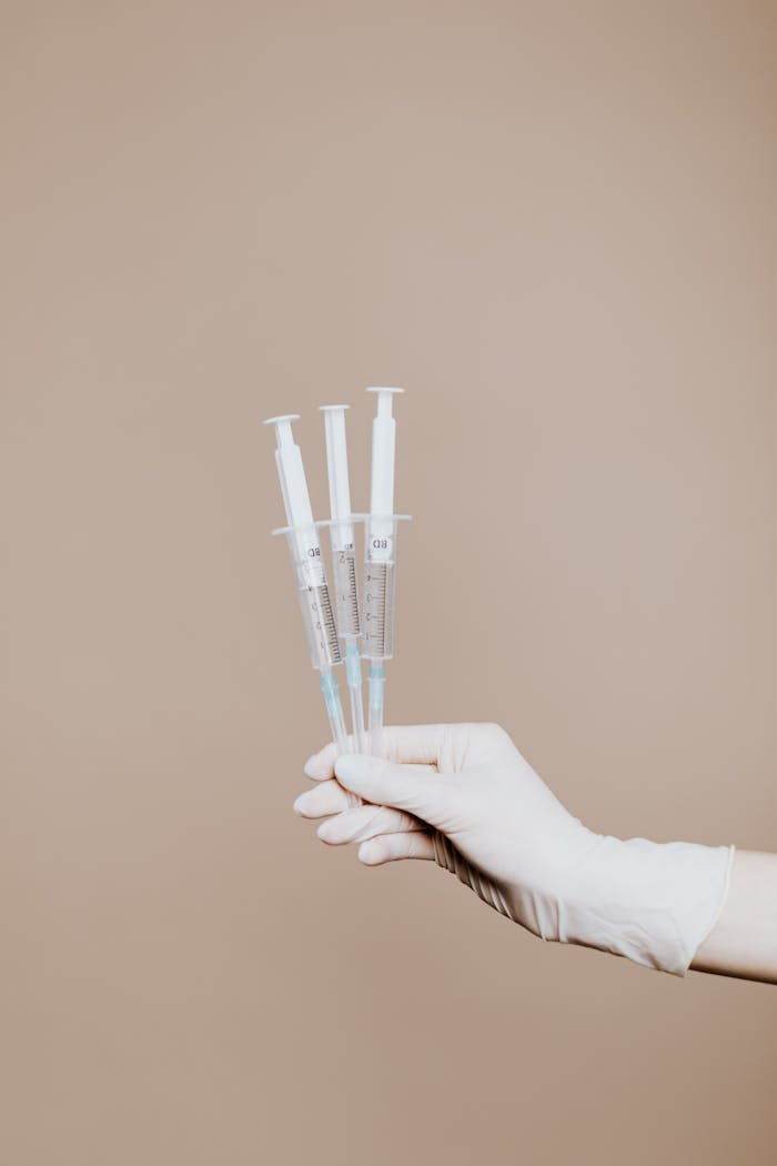 Gloved hand holding sterile syringes for medical use.