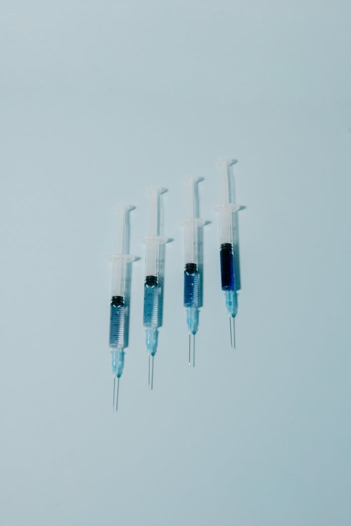 Contact A group of syringes with blue liquid on a light blue background, minimal and clinical.
